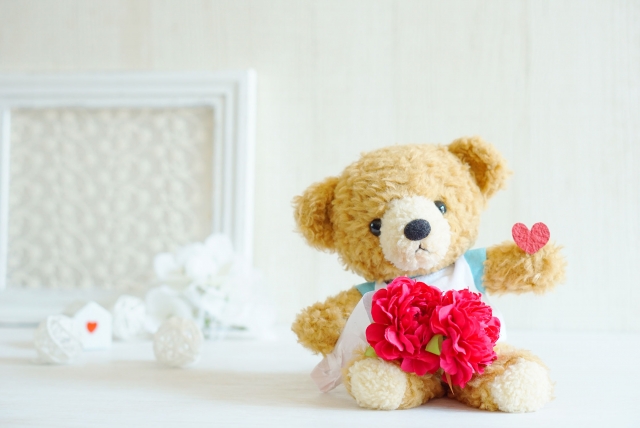 ハートを持ったくまのぬいぐるみとお花の写真